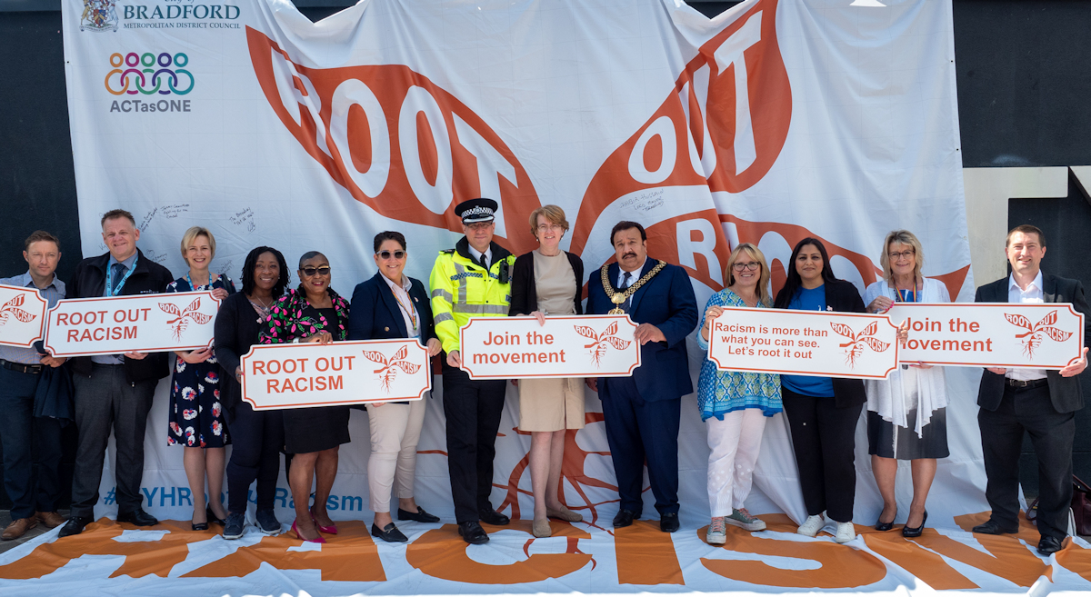 Kersten England with colleagues and VIP guests holding Root Out Racism signs at the Root Out Racism launch event in Bradford